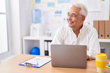 Ofiste çalışırken dizüstü bilgisayar kullanan orta yaşlı, kır saçlı bir iş adamı.