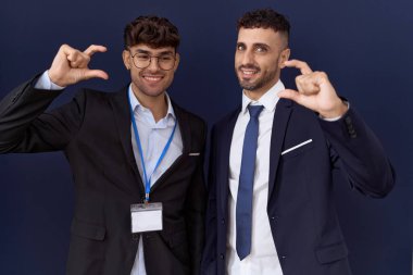 İki İspanyol iş adamı iş kıyafetleri giyip gülümsüyor ve el hareketleriyle el hareketi yapıyor parmaklarıyla işaret yapıyor ve kameraya bakıyor. ölçüm kavramı. 