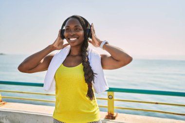 Afrika kökenli Amerikalı kadın spor giyer ve deniz kenarında müzik dinler.