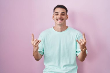 Yakışıklı İspanyol adam pembe arka planda duruyor çılgın bir ifadeyle bağırıyor elleri havada rock sembolü yapıyor. Müzik yıldızı. ağır müzik konsepti. 