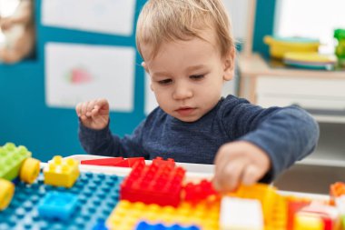 Anaokulundaki masada oturan sevimli sarışın çocuk inşaat bloklarıyla oynuyor.