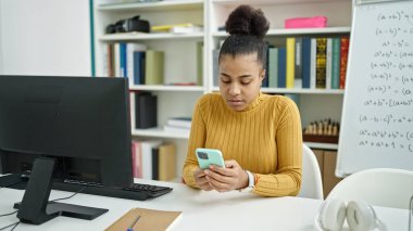 Genç Afrikalı Amerikalı bayan öğrenci kütüphanede akıllı telefon kullanıyor.