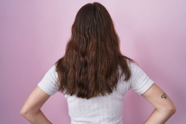 Pembe arka planda duran genç İspanyol kız kolları vücudunda geriye doğru bakıyor. 