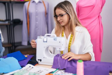 Elbise dükkanında dikiş makinesi kullanan kendine güvenen genç sarışın kadın terzi.
