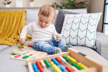 Abaküsle oynayan sevimli sarışın çocuk evdeki kanepede oturuyor.