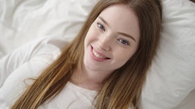 Genç sarışın kadın yatakta kendinden emin bir şekilde gülümsüyor.