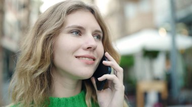 Young blonde woman smiling confident talking on the smartphone at coffee shop terrace