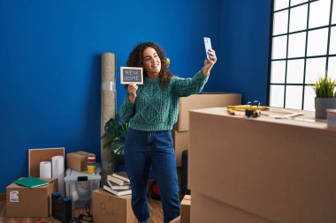 Genç ve güzel İspanyol kadın yeni evinde elinde karatahtayla akıllı telefonuyla selfie çekiyor.