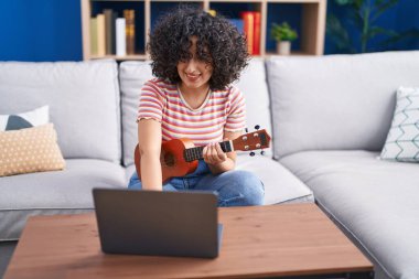 Ukulele dersi alan genç bir ortadoğu kadını evde yatakta oturuyor.