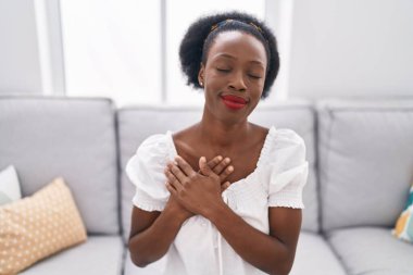 African american woman sitting on sofa with hands on chest at home