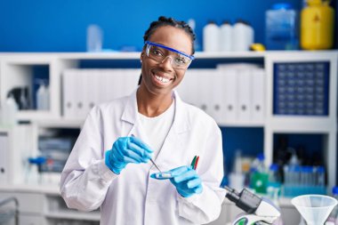 African american woman scientist smiling confident holding pills at laboratory