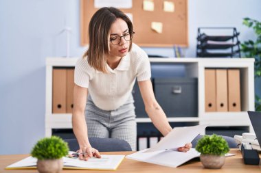 Young beautiful hispanic woman business worker reading document working at office