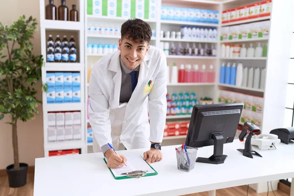 Fiatal Spanyol Férfi Gyógyszerész Mosolygós Magabiztos Írás Dokumentum Gyógyszertárban — Stock Fotó