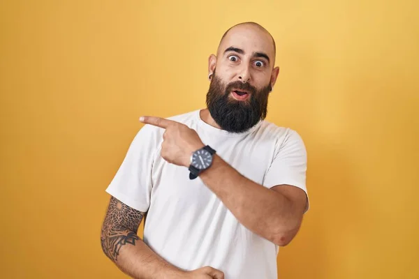 Young Hispanic Man Beard Tattoos Standing Yellow Background Surprised Pointing —  Fotos de Stock