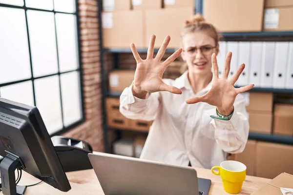 Young caucasian woman working at small business ecommerce using laptop afraid and terrified with fear expression stop gesture with hands, shouting in shock. panic concept.