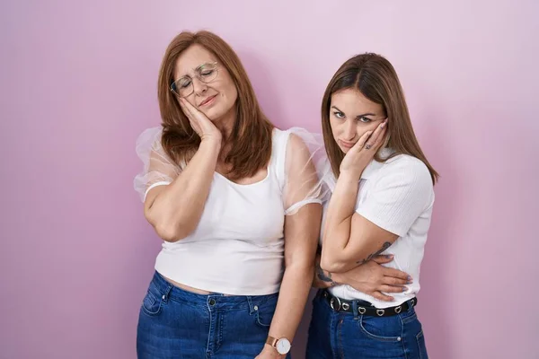 Hispanic mother and daughter wearing casual white t shirt over pink background thinking looking tired and bored with depression problems with crossed arms.
