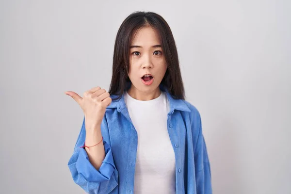 站在白色背景上的年轻中国女人惊讶地用手指头指向旁边 张开嘴惊讶的表情 — 图库照片