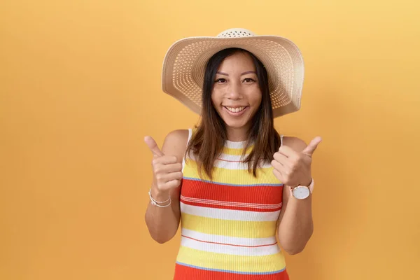 中年妇女戴着夏帽 头戴黄色背景的成功标志 手拿着积极的手势 竖起大拇指 笑逐颜开 快乐的表达和胜利的姿态 — 图库照片