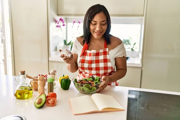 西班牙裔黑发女人在厨房里调味绿色沙拉 — 图库照片