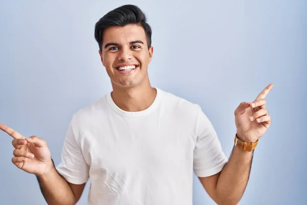 站在蓝色背景上的西班牙裔男子面带微笑 自信地用手指指向不同的方向 复制广告空间 — 图库照片