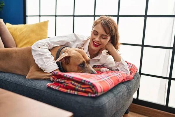 年轻的高加索女人笑着抱着一只自信的狗躺在家里的沙发上 — 图库照片
