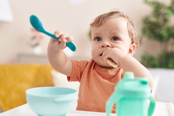 Adorable blond toddler sitting on highchair eating snack at home