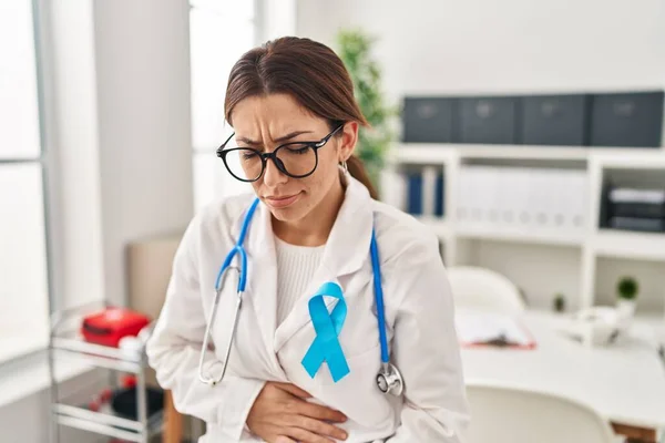 Young brunette doctor woman wearing stethoscope at the clinic with hand on stomach because nausea, painful disease feeling unwell. ache concept.