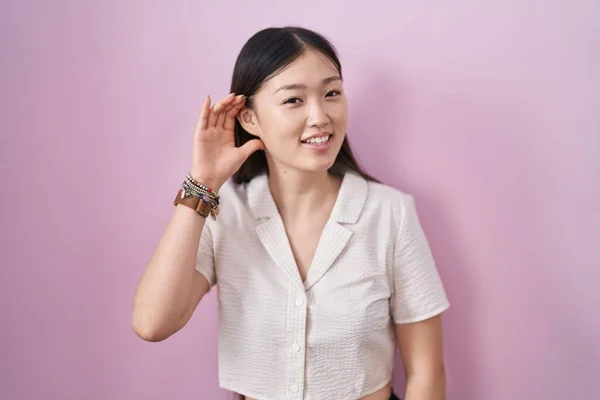 Chinese Young Woman Standing Pink Background Smiling Hand Ear Listening — Stockfoto