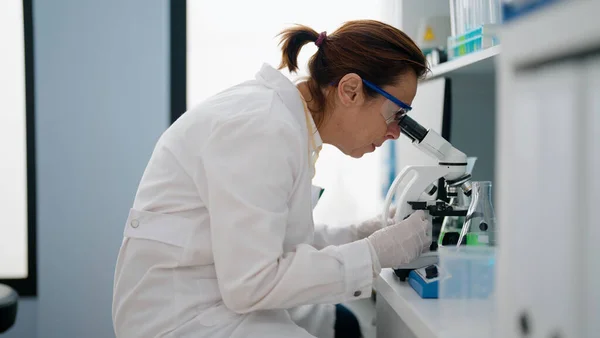 stock image Middle age hispanic woman wearing scientist uniform using microscope at laboratory