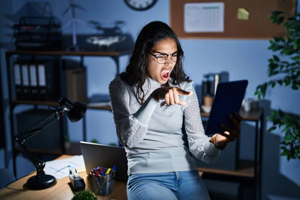 Stock image Young brazilian woman using touchpad at night working at the office pointing displeased and frustrated to the camera, angry and furious with you 