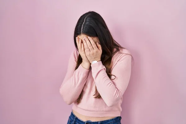 年轻的黑发女子站在粉红的背景上 脸上挂着忧郁的表情 一边哭一边用手捂住脸 抑郁症的概念 — 图库照片