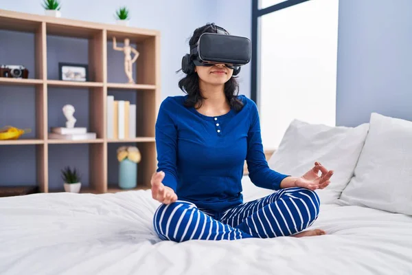 Yatak odasında sanal gerçeklik gözlüğü kullanarak yoga yapan genç Latin kadın.