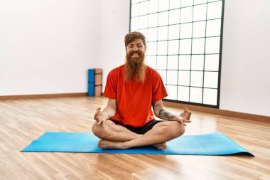 Genç kızıl saçlı, gülümseyen, spor merkezinde yoga eğitimi alan kendine güvenen bir adam.
