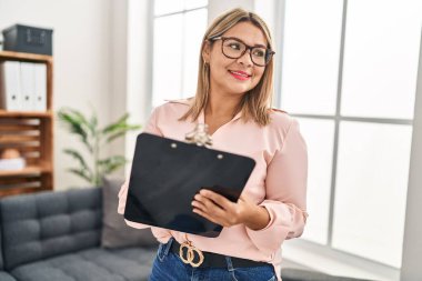 Young hispanic woman holding clipboard having psychology session psychology center