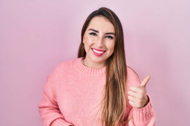 Pembe arka planda duran genç İspanyol kadın elleriyle mutlu bir jest yapıyor. Kameraya bakıp başarıyı gösteren ifade. 