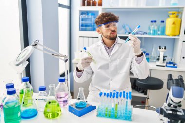 Young arab man scientist measuring liquid holding test tubes at laboratory