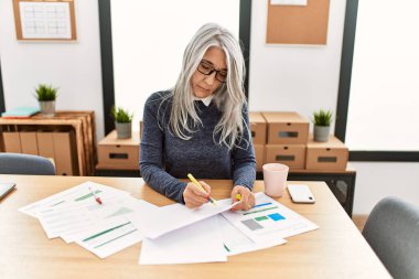 Ofiste çalışırken gülümseyen beyaz saçlı iş kadını.