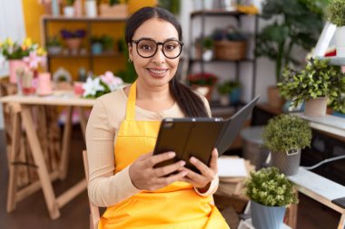 Young arab woman florist smiling confident using touchpad at flower shop