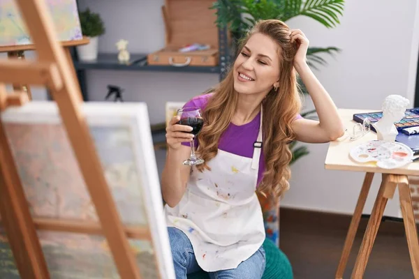 Young blonde woman artist drinking wine looking draw at art studio
