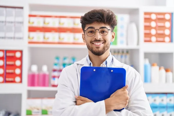 Joven Hombre Árabe Farmacéutico Sonriendo Confiado Abrazando Portapapeles Farmacia — Foto de Stock