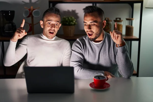 Homosexual couple using computer laptop pointing finger up with successful idea. exited and happy. number one.