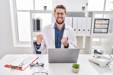 Doktor üniforması ve steteskop giymiş İspanyol bir adam kolları havada ve gözleri kapalı bir şekilde başarıyı kutluyor ve şaşırıyor. 