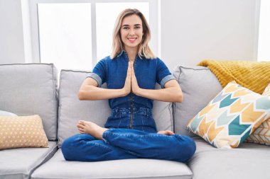 Yoga egzersizi yapan genç bir kadın evdeki kanepede oturuyor.