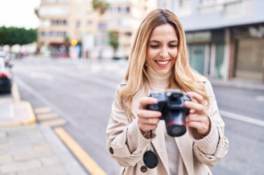 Young blonde woman smiling confident using professional camera at street