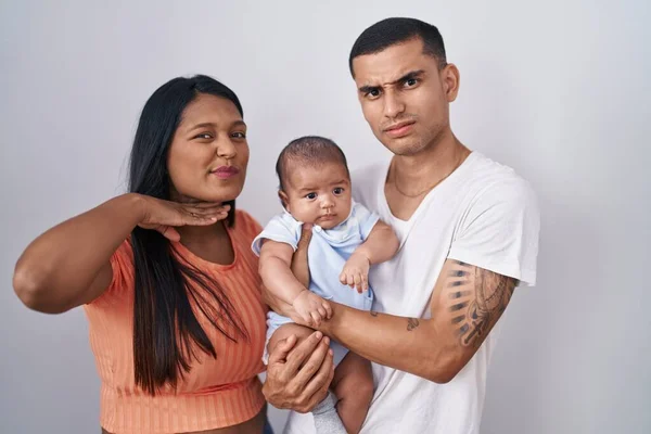 Young hispanic couple with baby standing together over isolated background cutting throat with hand as knife, threaten aggression with furious violence