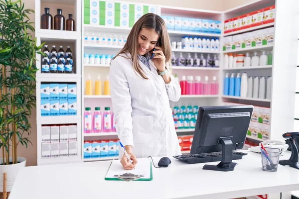 Young Beautiful Hispanic Woman Pharmacist Talking Smartphone Writing Document Pharmacy — Stockfoto