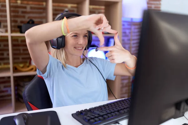 Young caucasian woman playing video games wearing headphones smiling making frame with hands and fingers with happy face. creativity and photography concept.
