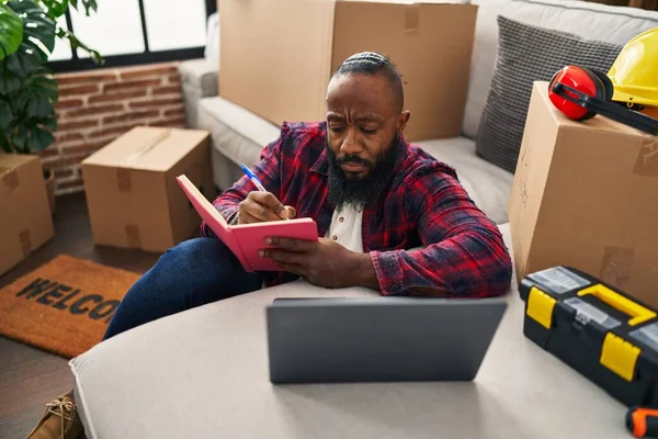 Young African American Man Using Laptop Writing Book Sitting Floor — стокове фото