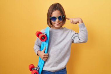 Güneş gözlüğü takan küçük İspanyol çocuk mutlu ve gururlu gülümseyen bir kişiyi işaret ediyor. 