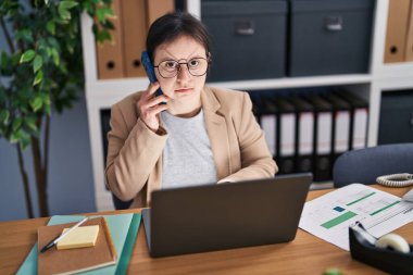 Down sendromlu genç bir kadın ofis telefonunda dizüstü bilgisayar kullanıyor.